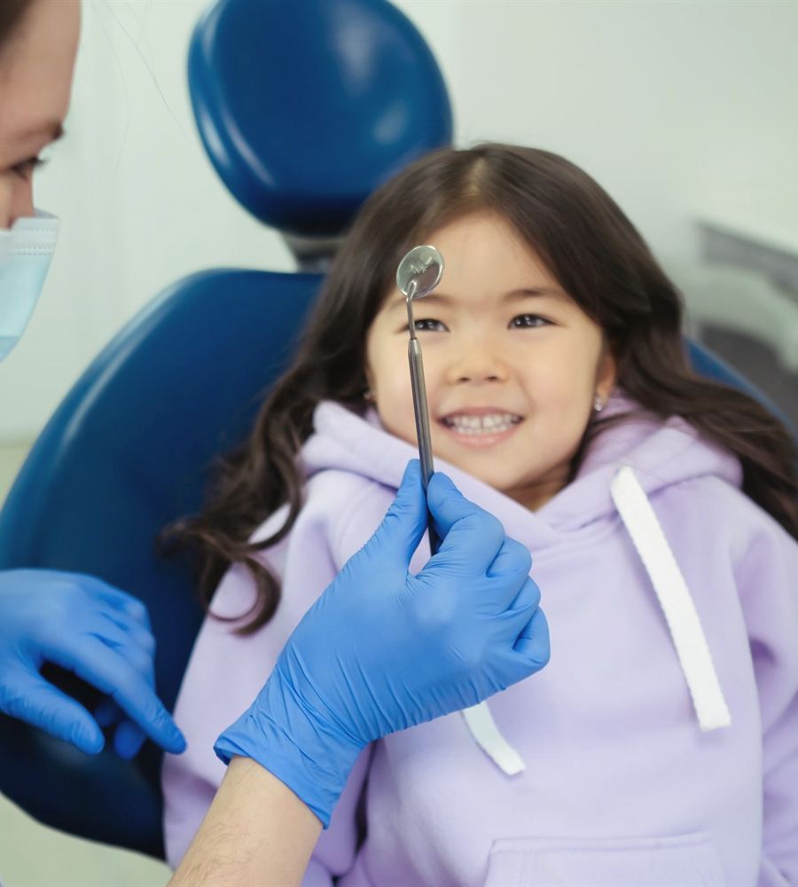 Dentista mostrando el espejo dental a una niña que sonríe